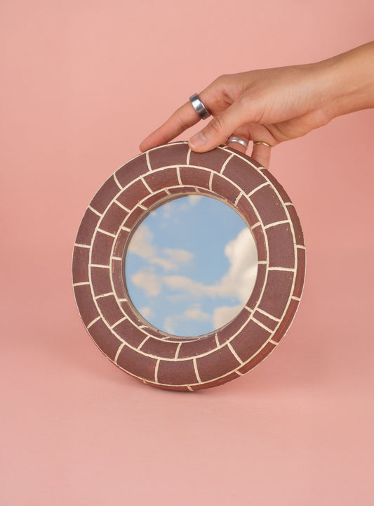 Handcrafted ceramic mirror with brick-patterned frame reflecting sky and clouds